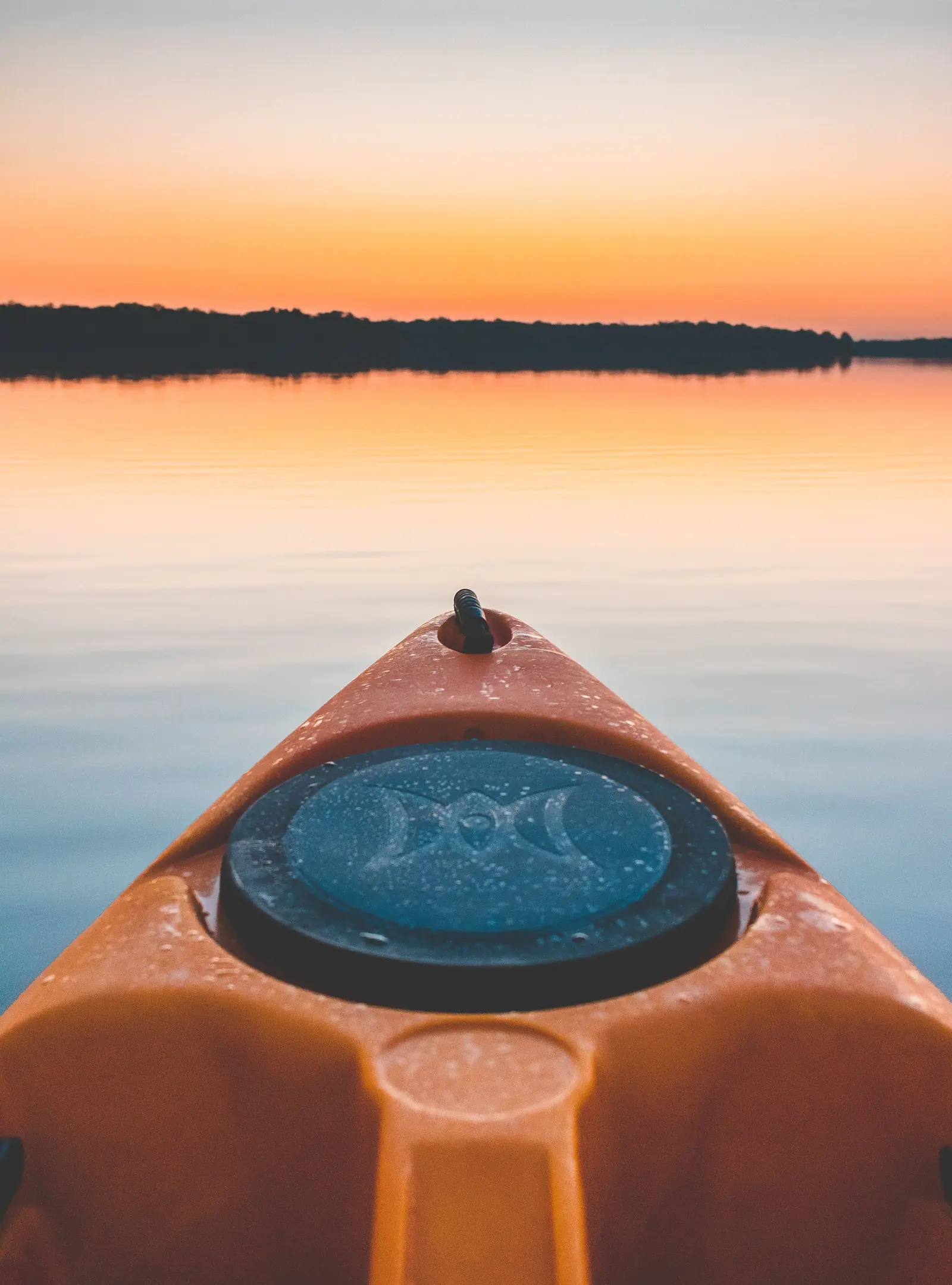 Bow of an orange kayak on calm water at sunrise